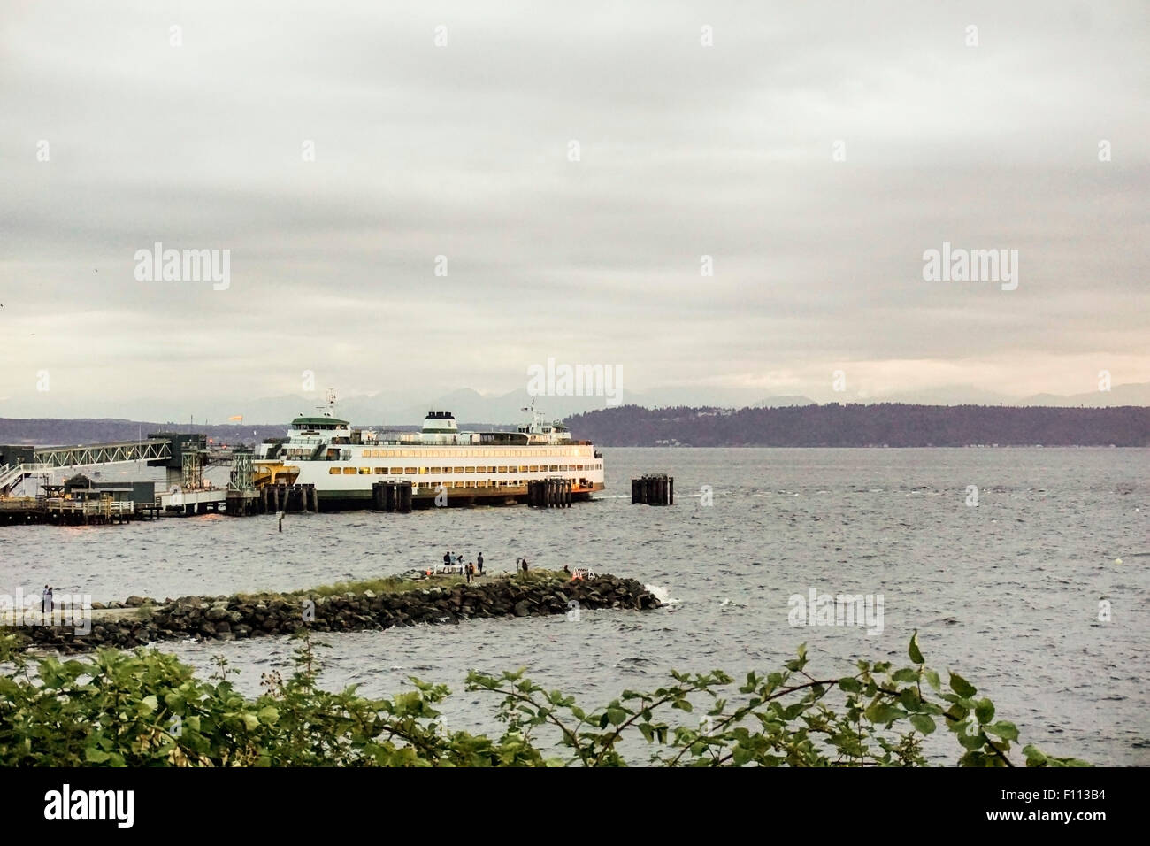 Voir d'Edmonds Puget sound waterfront comme les gens sur la jetée de pierre regarder le coucher du soleil avec le ferry à quai, la péninsule Olympique à distance Banque D'Images