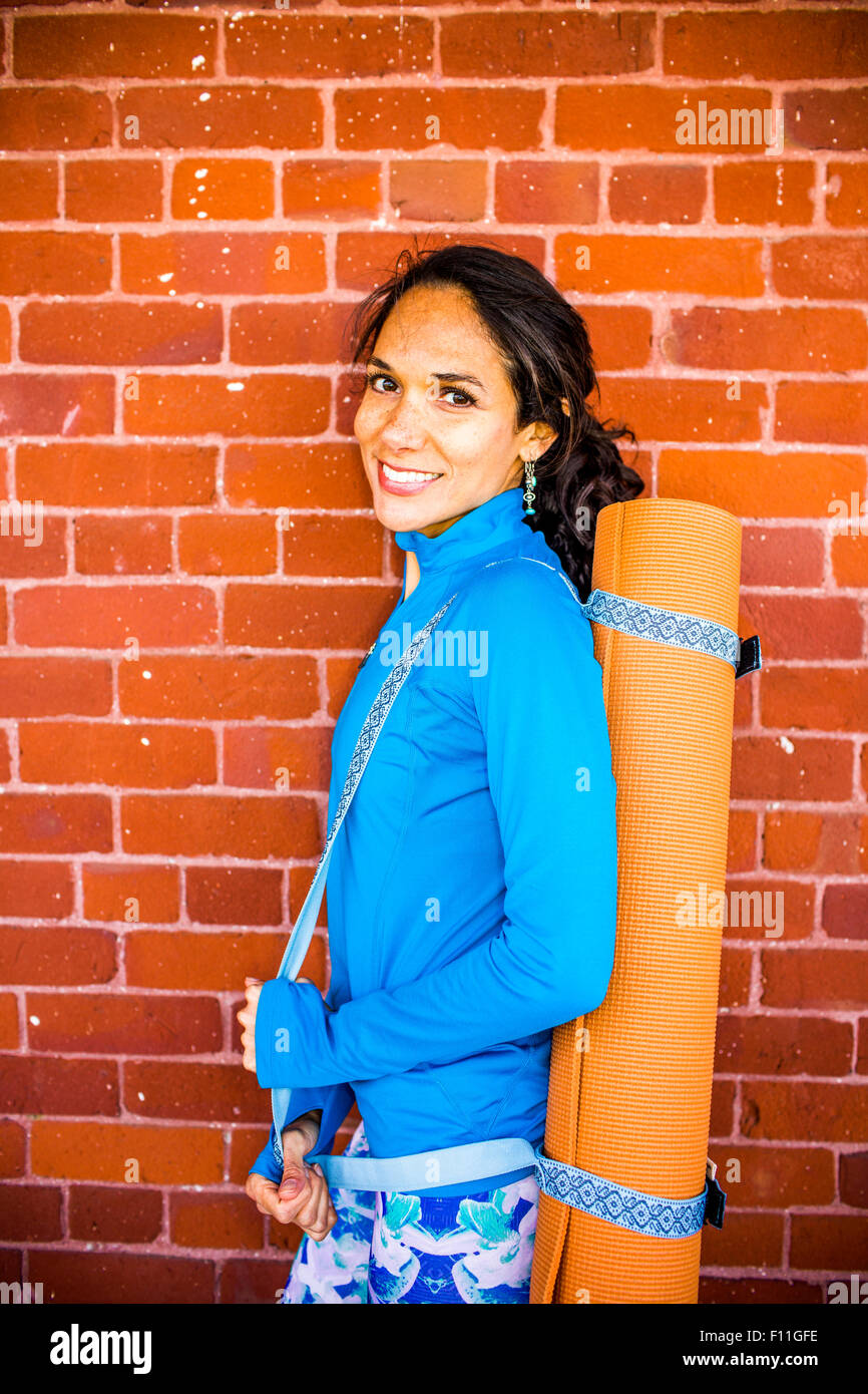 Hispanic woman carrying yoga mat au mur de brique Banque D'Images