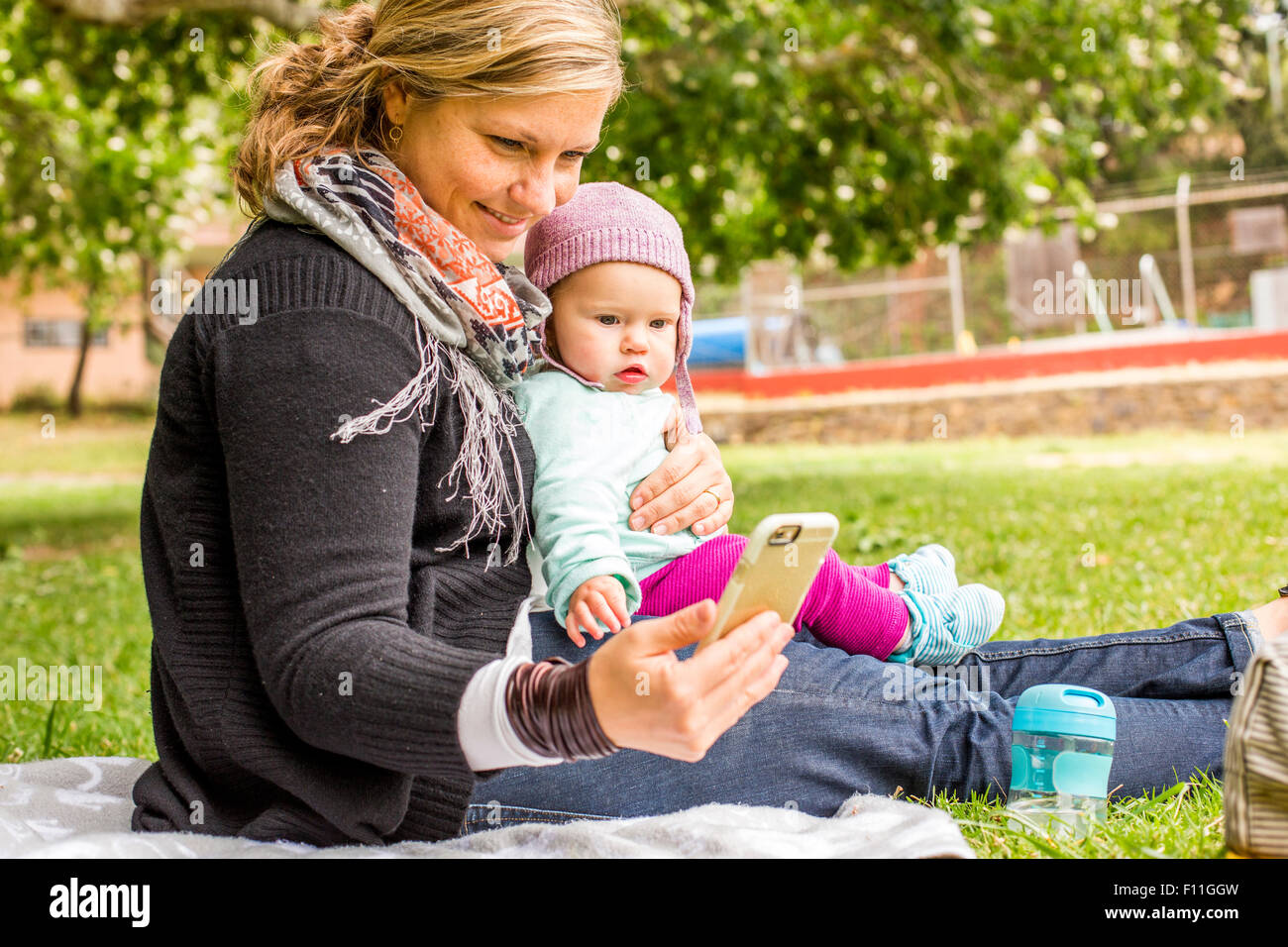Mère et fille bébé caucasien using cell phone in park Banque D'Images