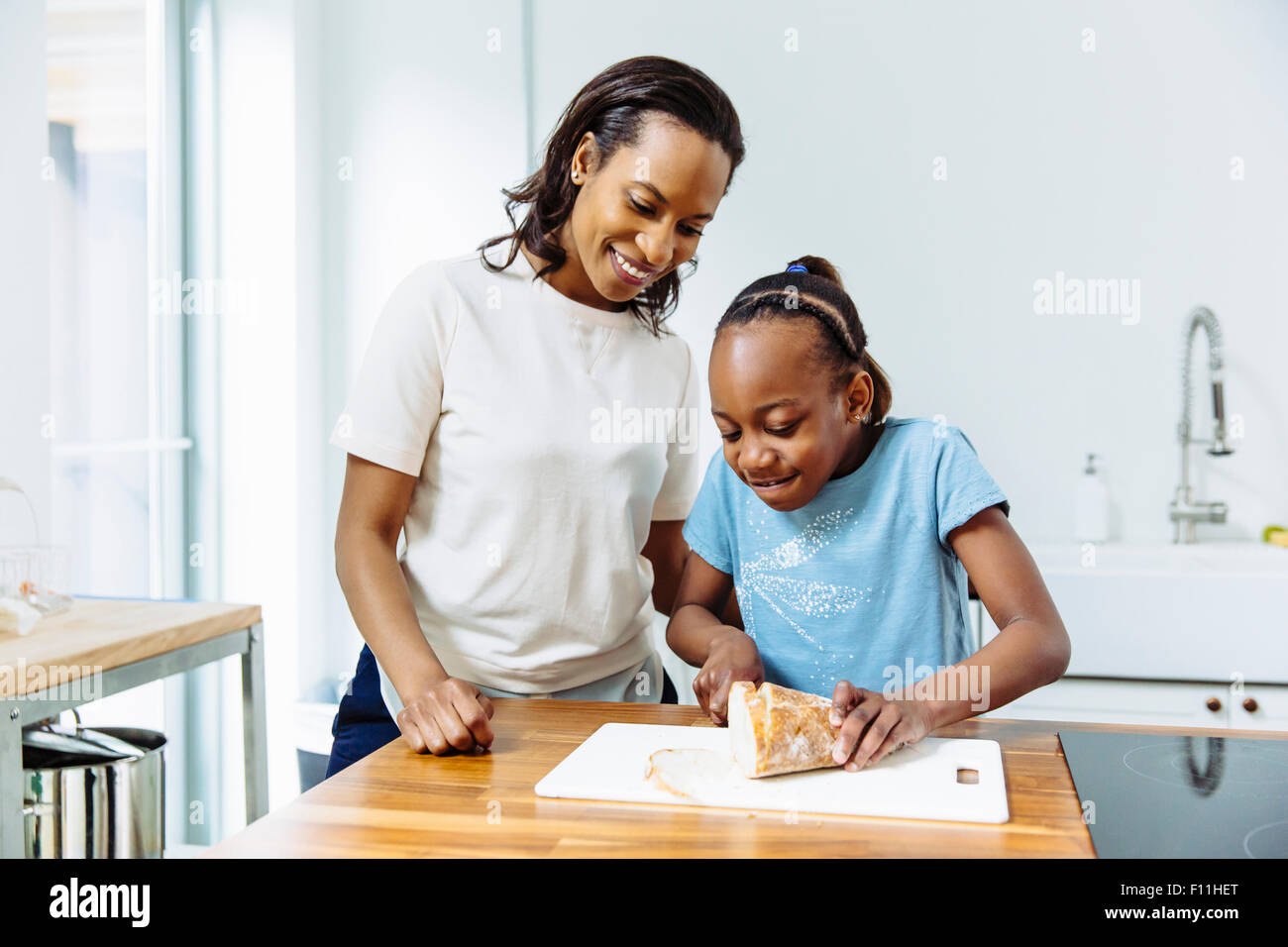 La mère et la fille noire du pain en tranches dans la cuisine Banque D'Images