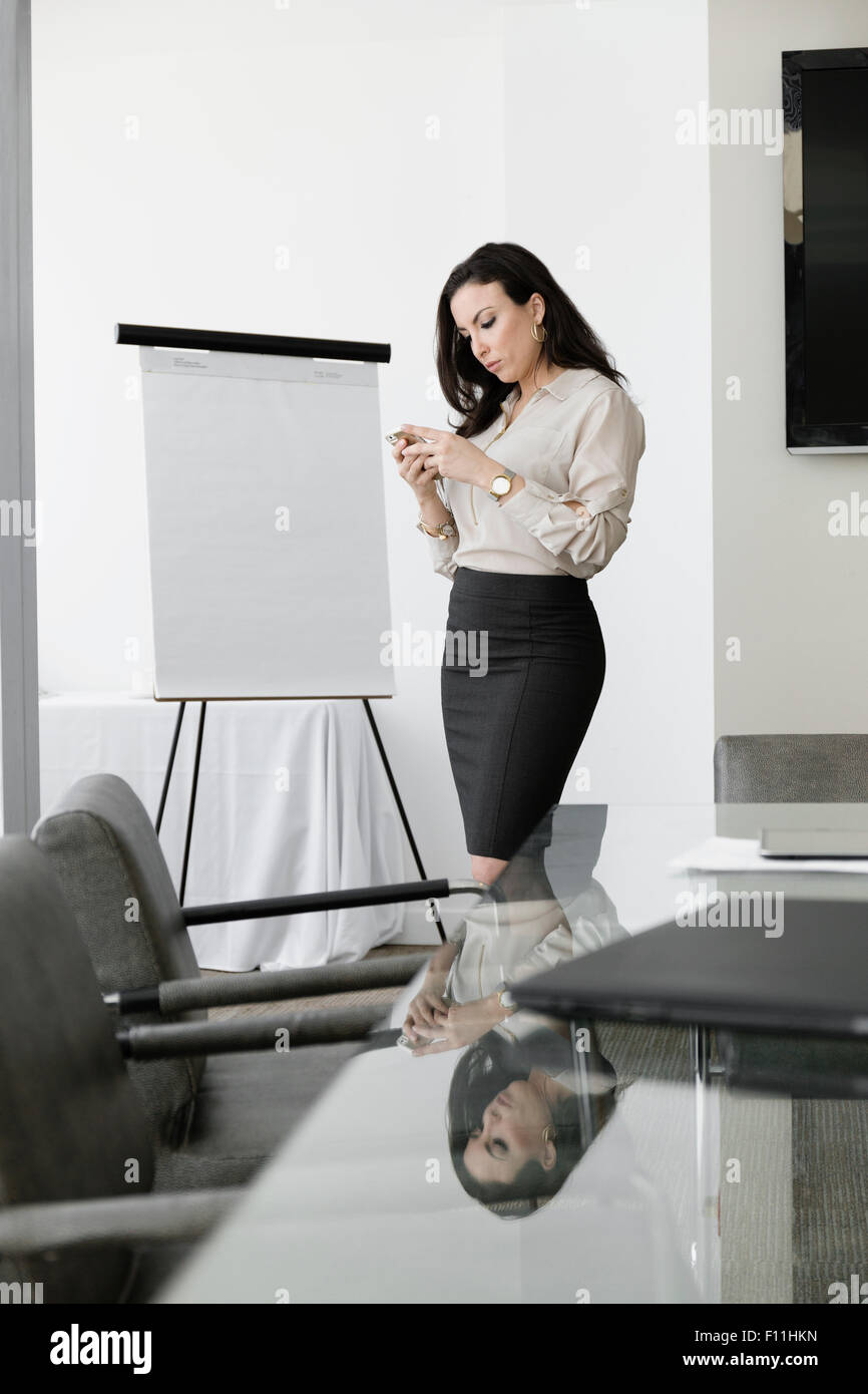 Mixed Race businesswoman using cell phone in conference room Banque D'Images