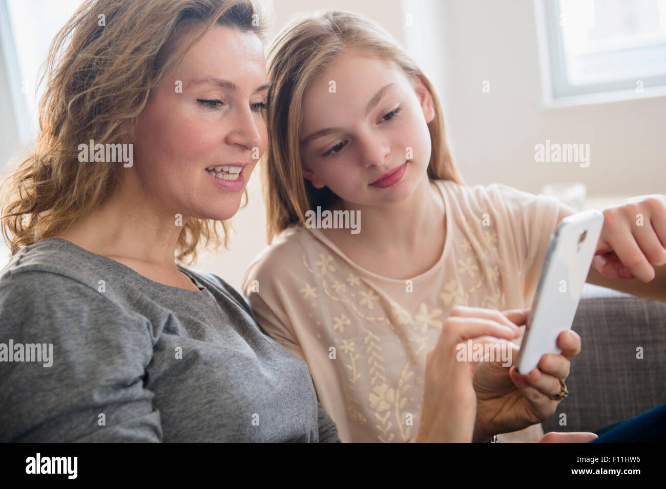 Caucasian mother and daughter using cell phone in living room Banque D'Images