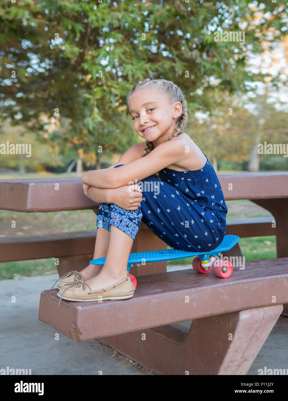 Mixed Race girl sitting on skateboard sur une table de pique-nique Banque D'Images
