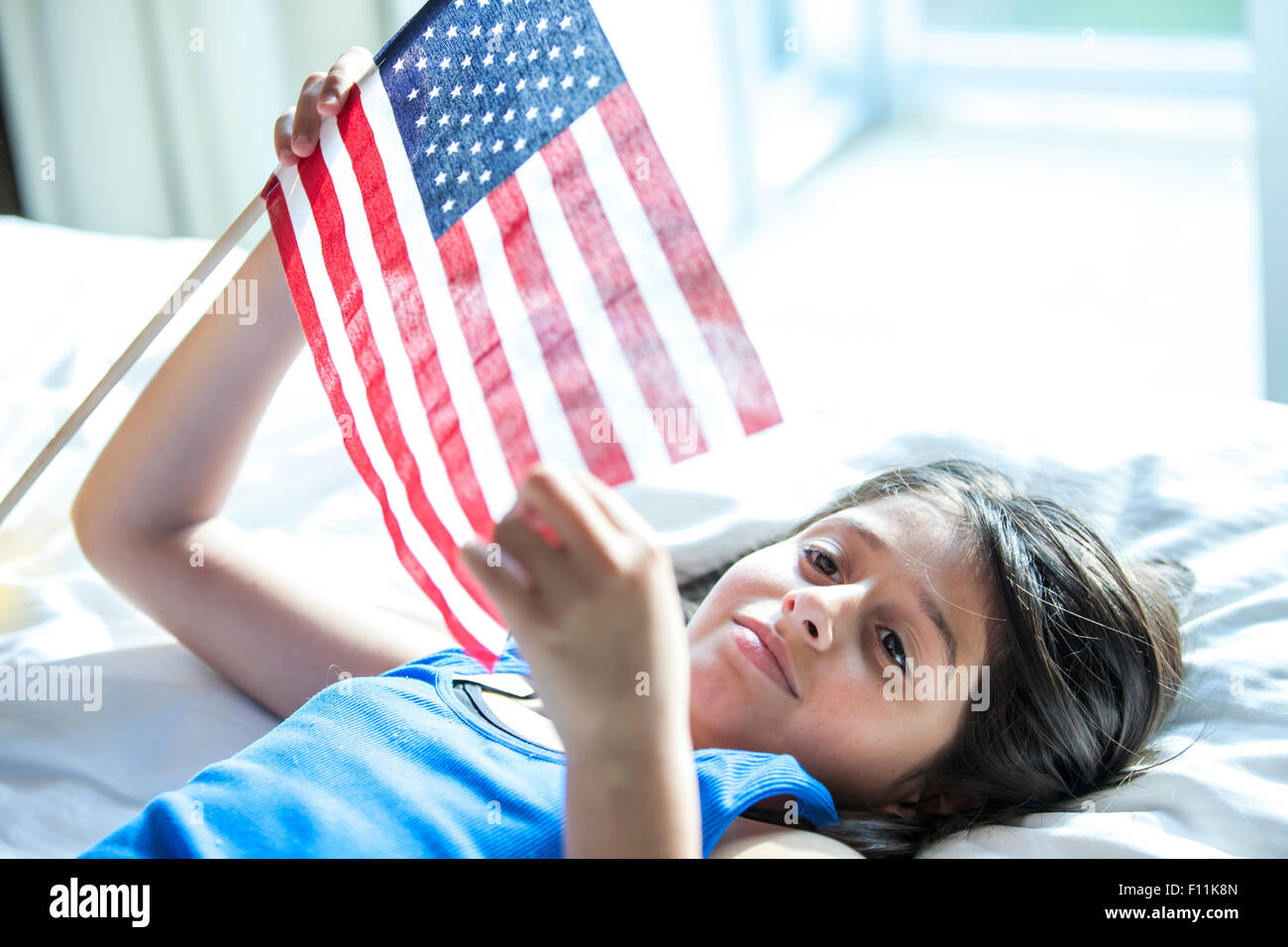 Hispanic girl holding American flag on bed Banque D'Images