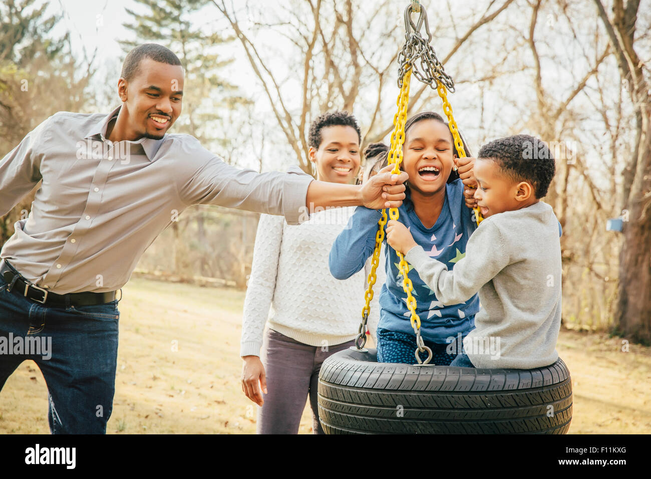 La famille noire jouant sur balançoire pneu Banque D'Images