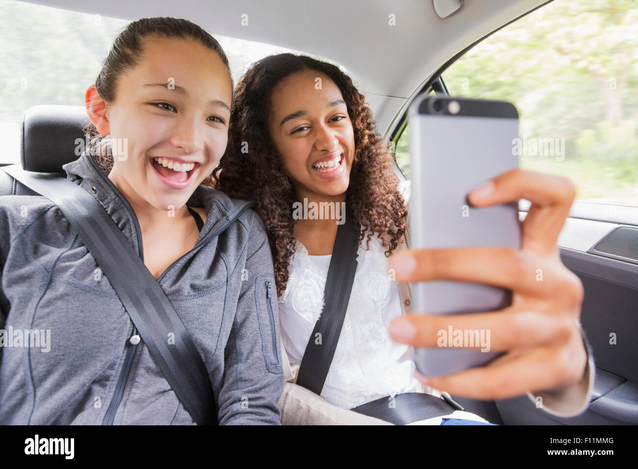 Teenage Girls using cell phone in car siège arrière Banque D'Images