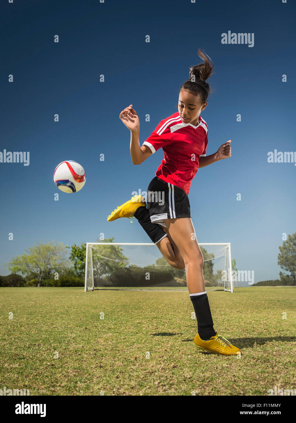 Race mixte soccer player kicking ball on field Banque D'Images