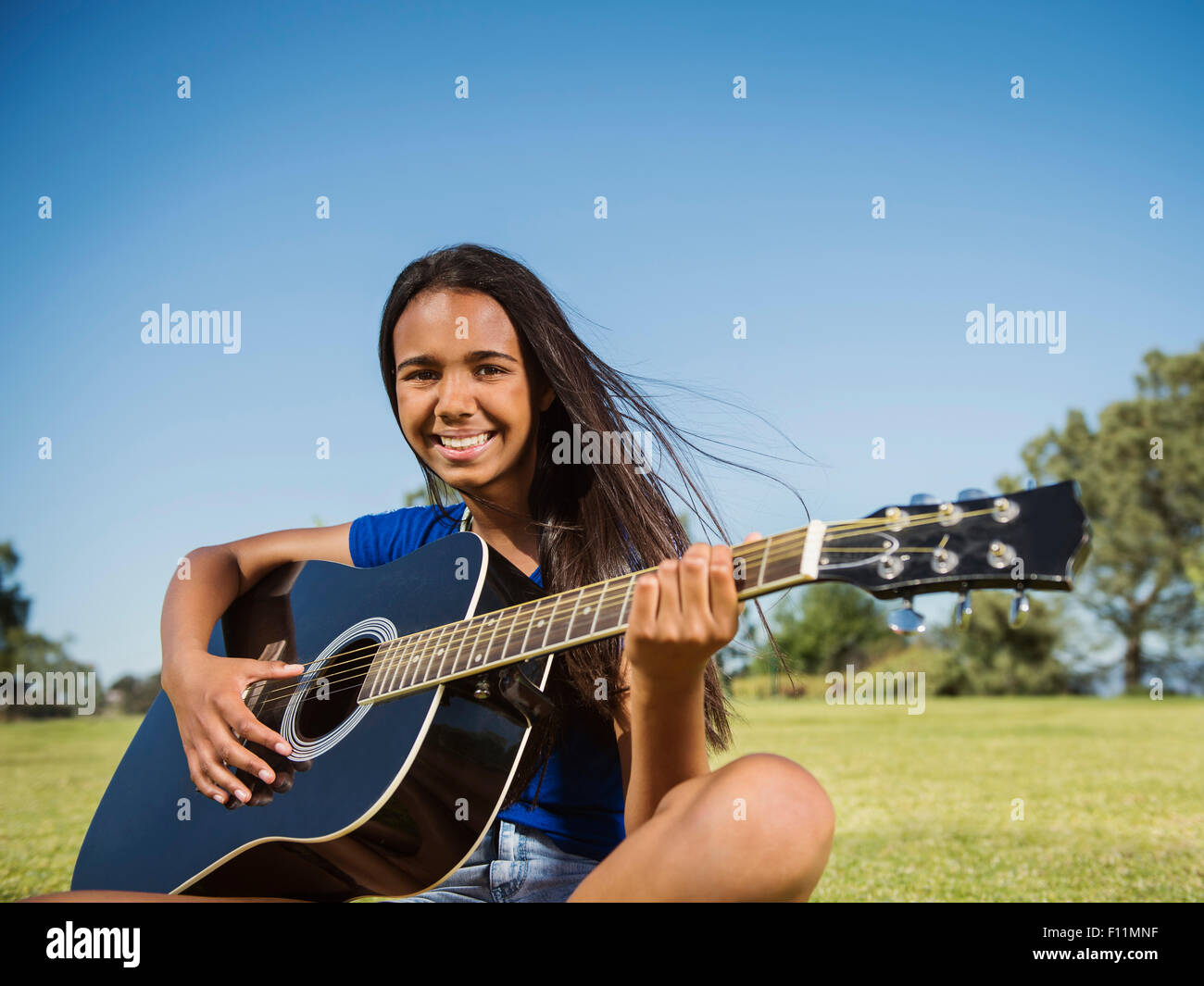Mixed Race girl playing guitar in park Banque D'Images