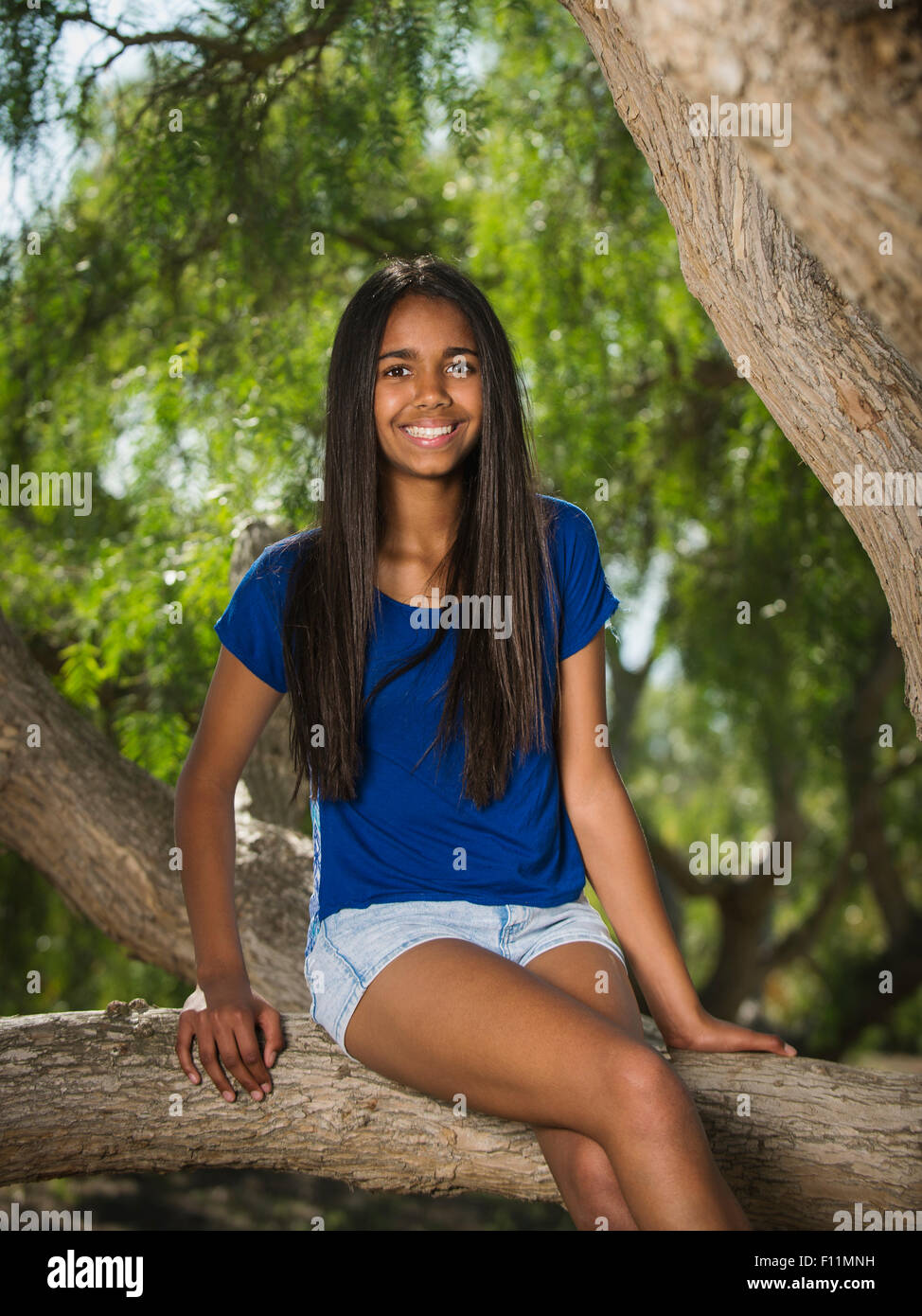 Mixed Race girl sitting on tree branch Banque D'Images