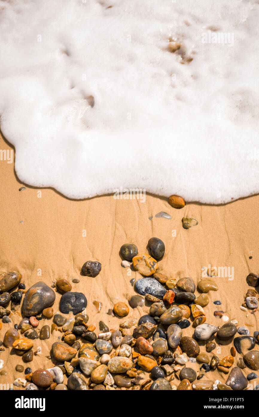 Une vague se lave plus de cailloux sur une plage de Suffolk. Banque D'Images