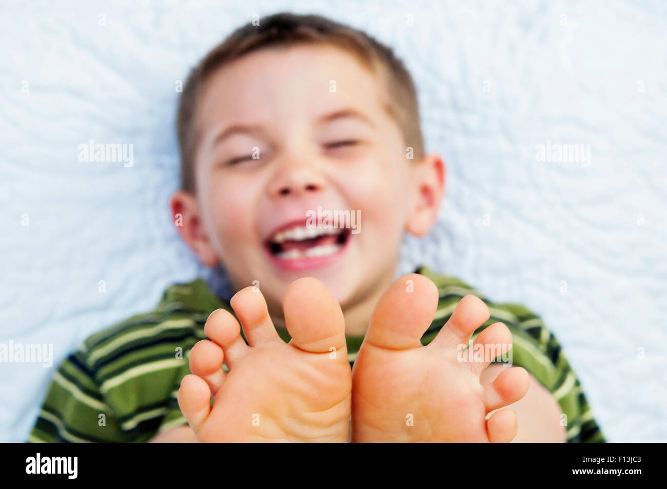 Petit garçon rit sur lit avec tickly orteils pieds nus Banque D'Images