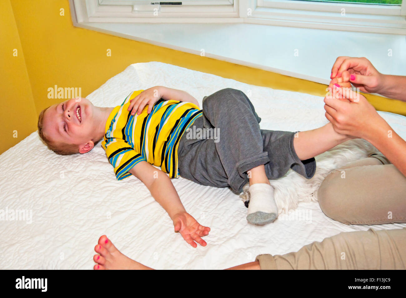 Lit enfant jette sur rire lors de l'obtention de son pied chatouillé Banque D'Images