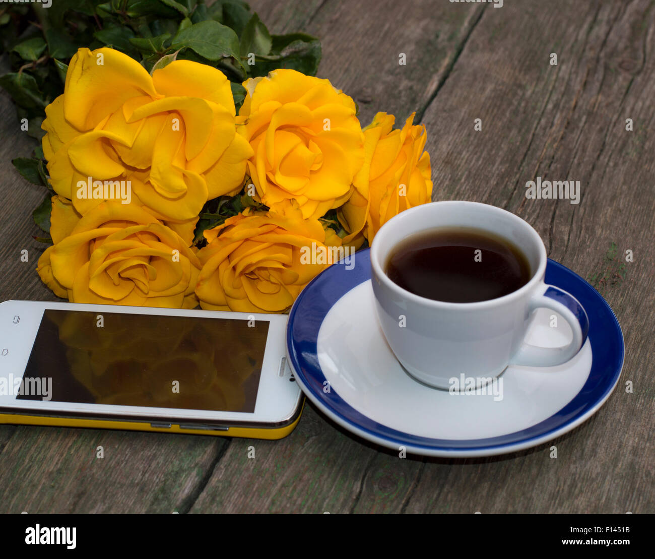 Le café, des roses jaunes et le téléphone mobile sur une table en bois Banque D'Images