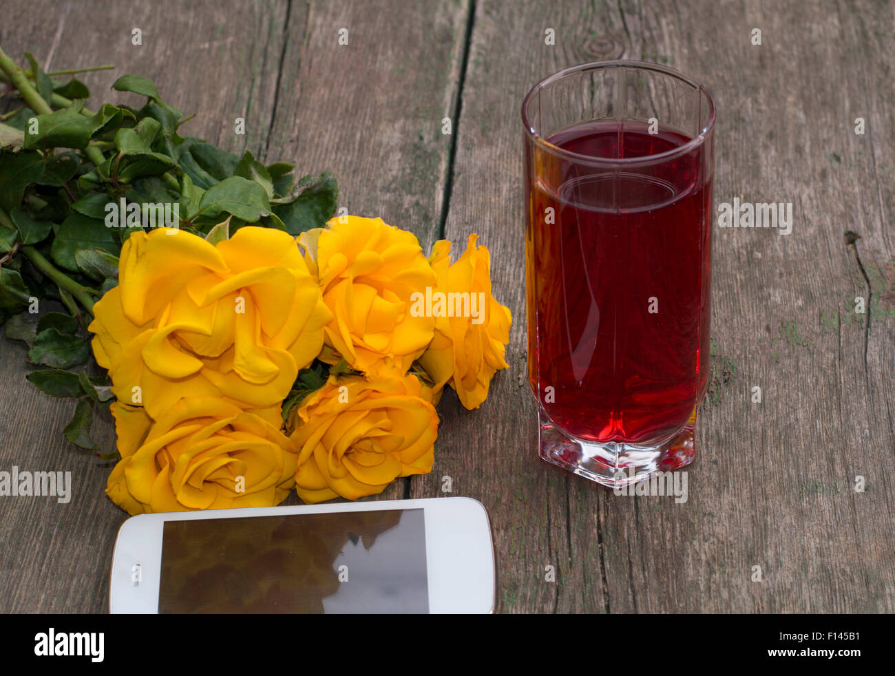 Des roses jaunes, le téléphone mobile et le verre de jus sur une table en bois Banque D'Images