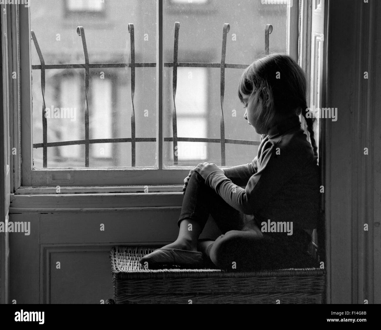 1960 SAD LONELY GIRL À LA VILLE PAR L'INTERMÉDIAIRE DE VACANCES FENÊTRE AVEC BARRES DE SÉCURITÉ EN MÉTAL Banque D'Images