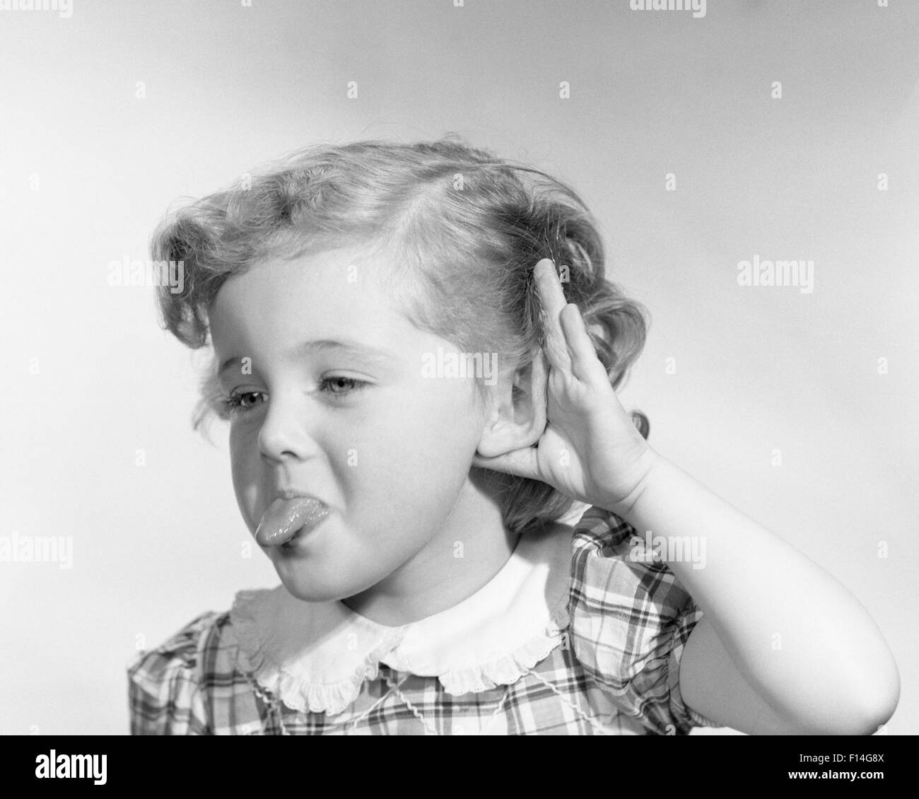 1950 Petite fille faisant des gestes grossiers STICKING OUT TONGUE PRENANT PART ON EAR Banque D'Images