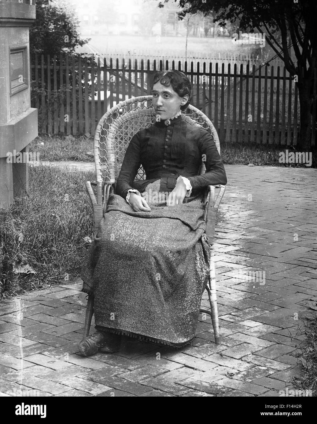 Années 1890 Années 1900 DÉBUT DU 20ème siècle SÉVÈRE PORTRAIT WOMAN SITTING IN WICKER CHAIR IN BACKYARD PAR CHAMBRE Banque D'Images