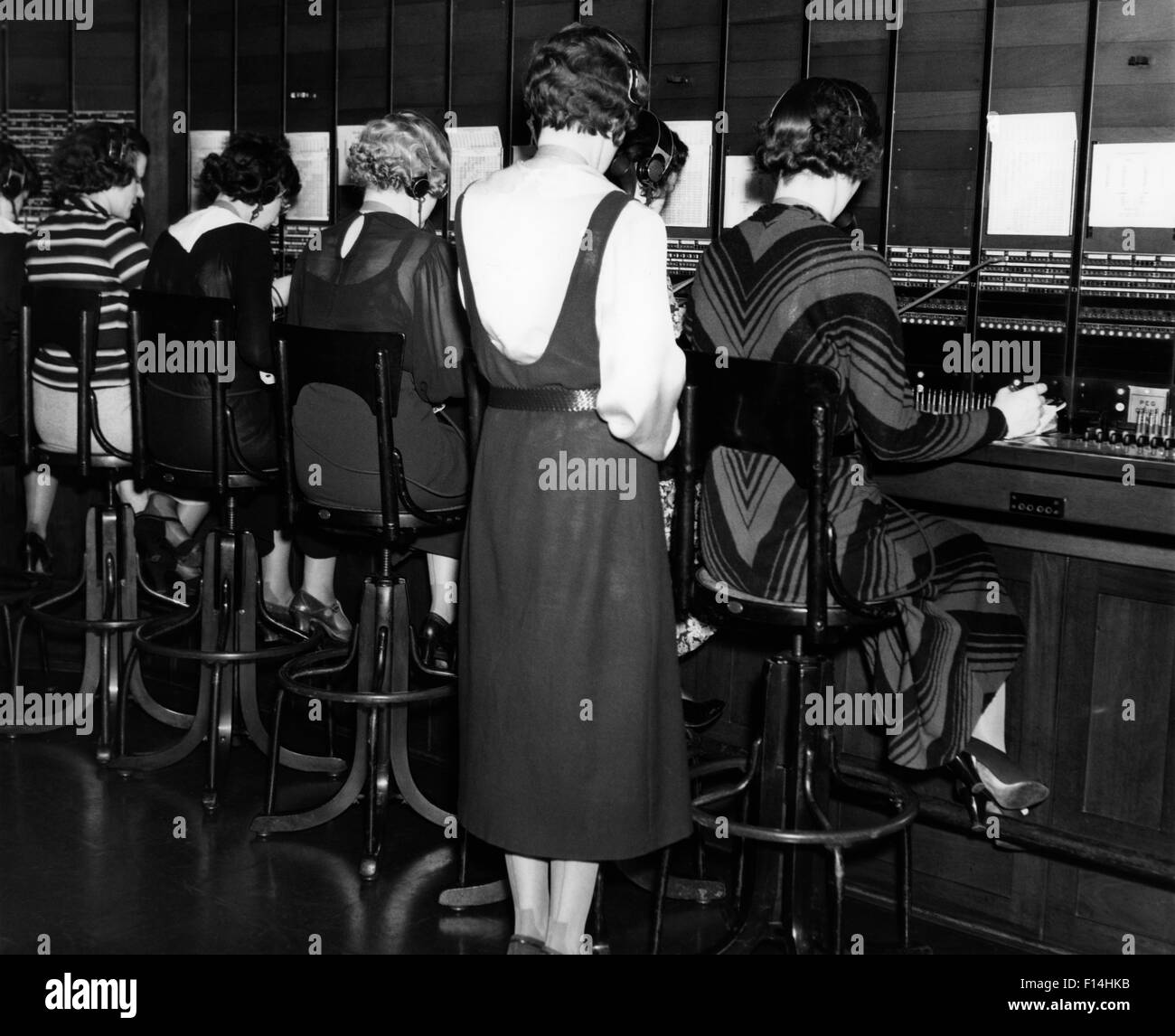 1930 VUE ARRIÈRE DE STANDARDISTES FEMMES ASSIS ET SUPERVISEUR PERMANENT Banque D'Images