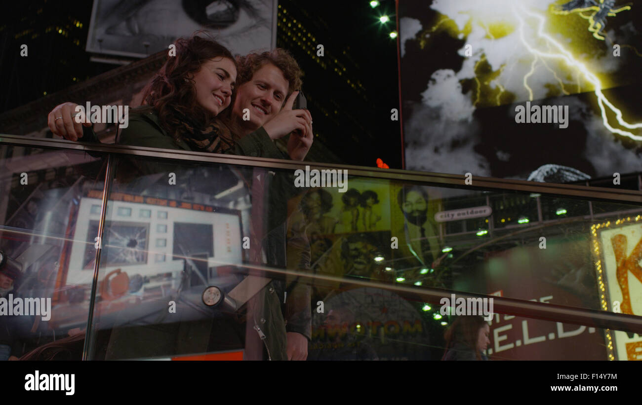 Low angle view of couple sur balcon photographier les panneaux publicitaires en ville emblématique intersection dans la nuit Banque D'Images