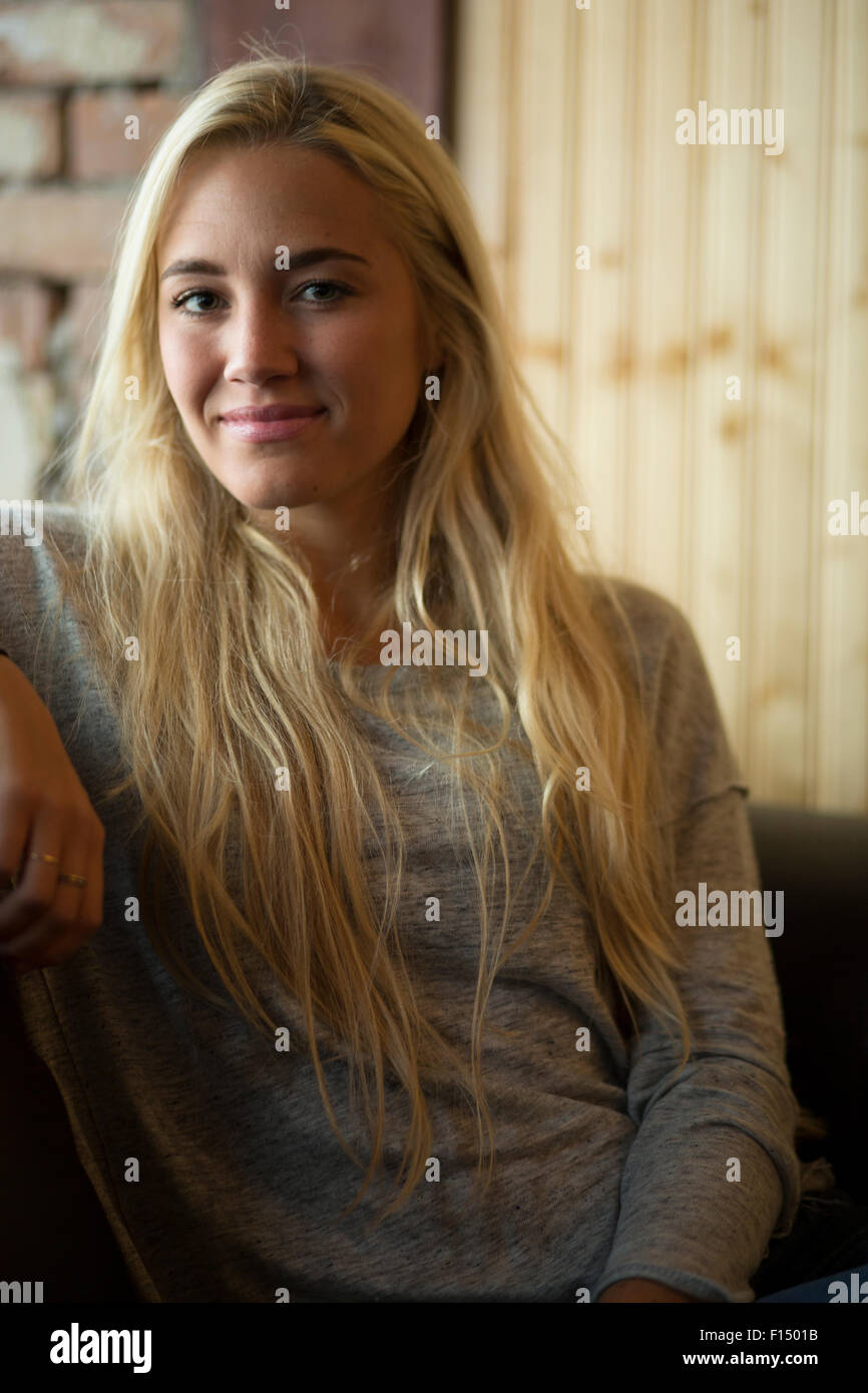 Femme heureuse avec de longs cheveux blonds sitting on sofa Banque D'Images