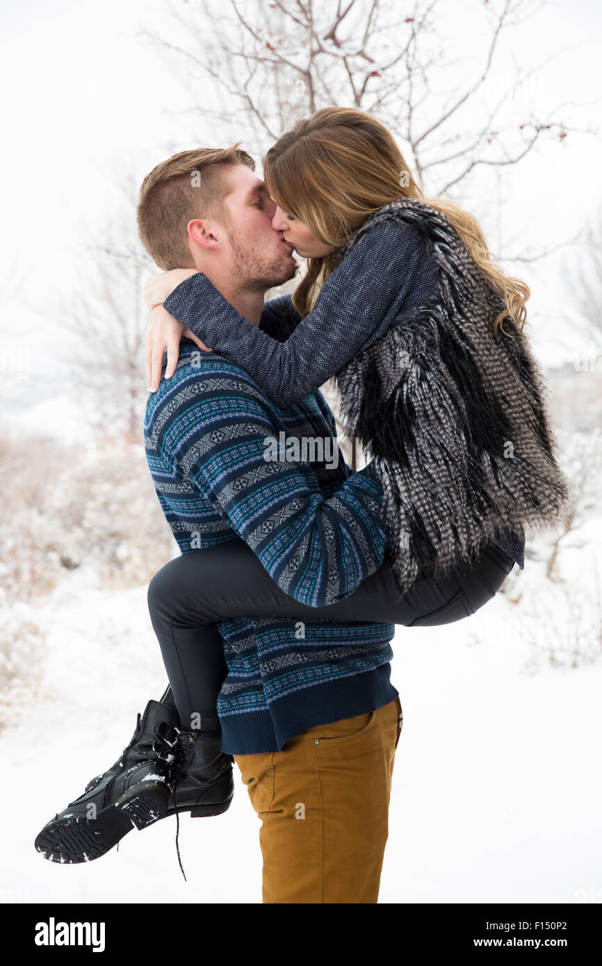 Vue latérale d'happy man holding et les baisers petite amie dans la neige Banque D'Images