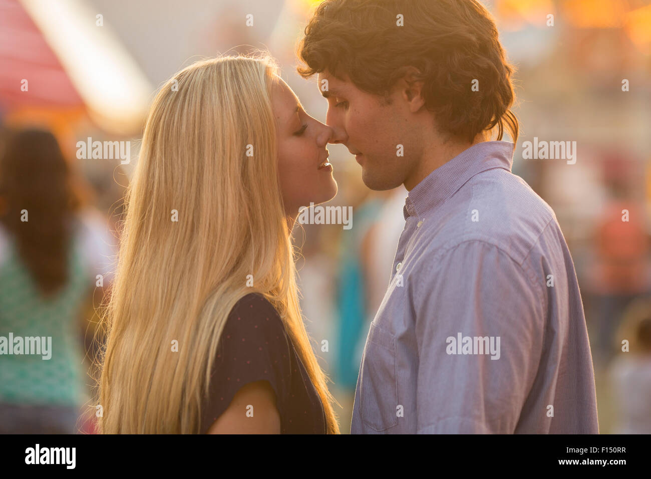 Profil des baisers rétroéclairé couple standing in amusement park amusement juste au coucher du soleil Banque D'Images