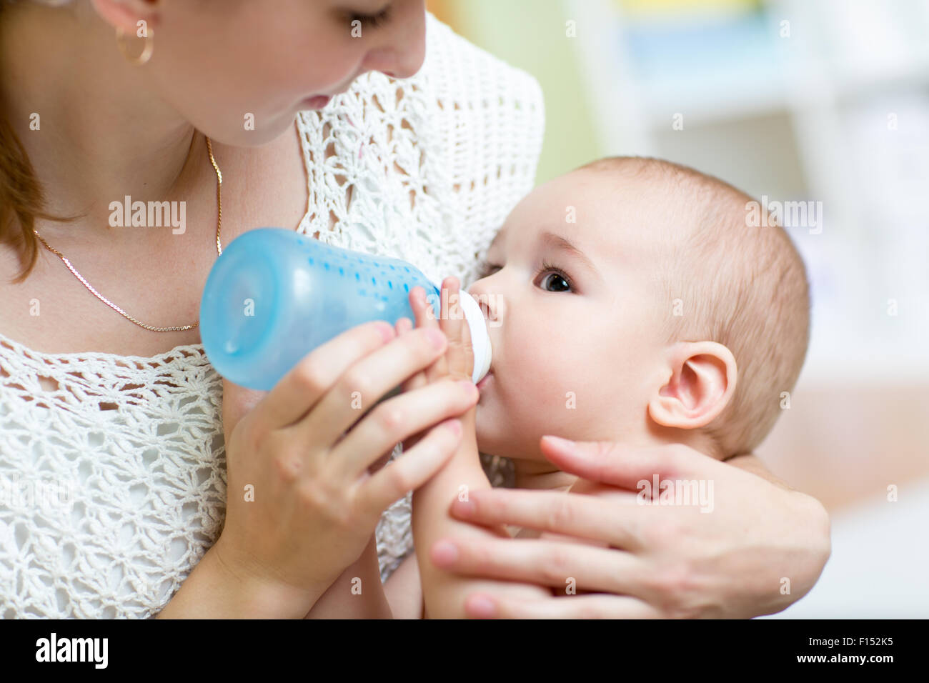 Jeune maman à la maison nourrir bébé avec une bouteille de lait, se sentant fier Banque D'Images