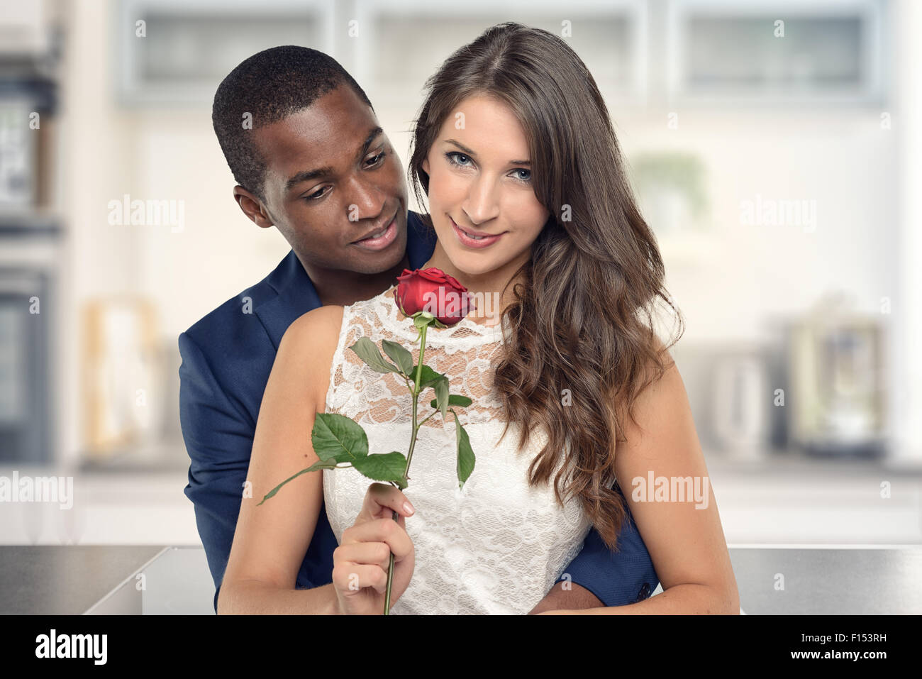 Beau Black American Boyfriend serrant sa jolie petite amie avec Fleur Rose et souriant à la caméra, debout dans l'kitc Banque D'Images