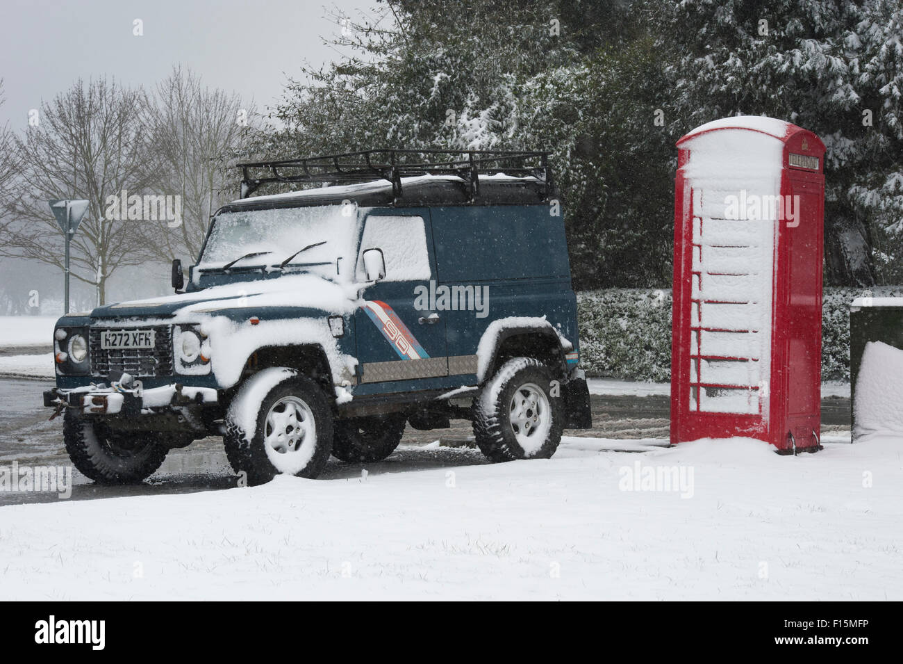 Deux icônes britanniques couvert de neige blanche - Land Rover Defender 90 garé à côté d'un téléphone rouge anglais fort sur une journée d'hiver enneigée - Ilkley, England, UK. Banque D'Images