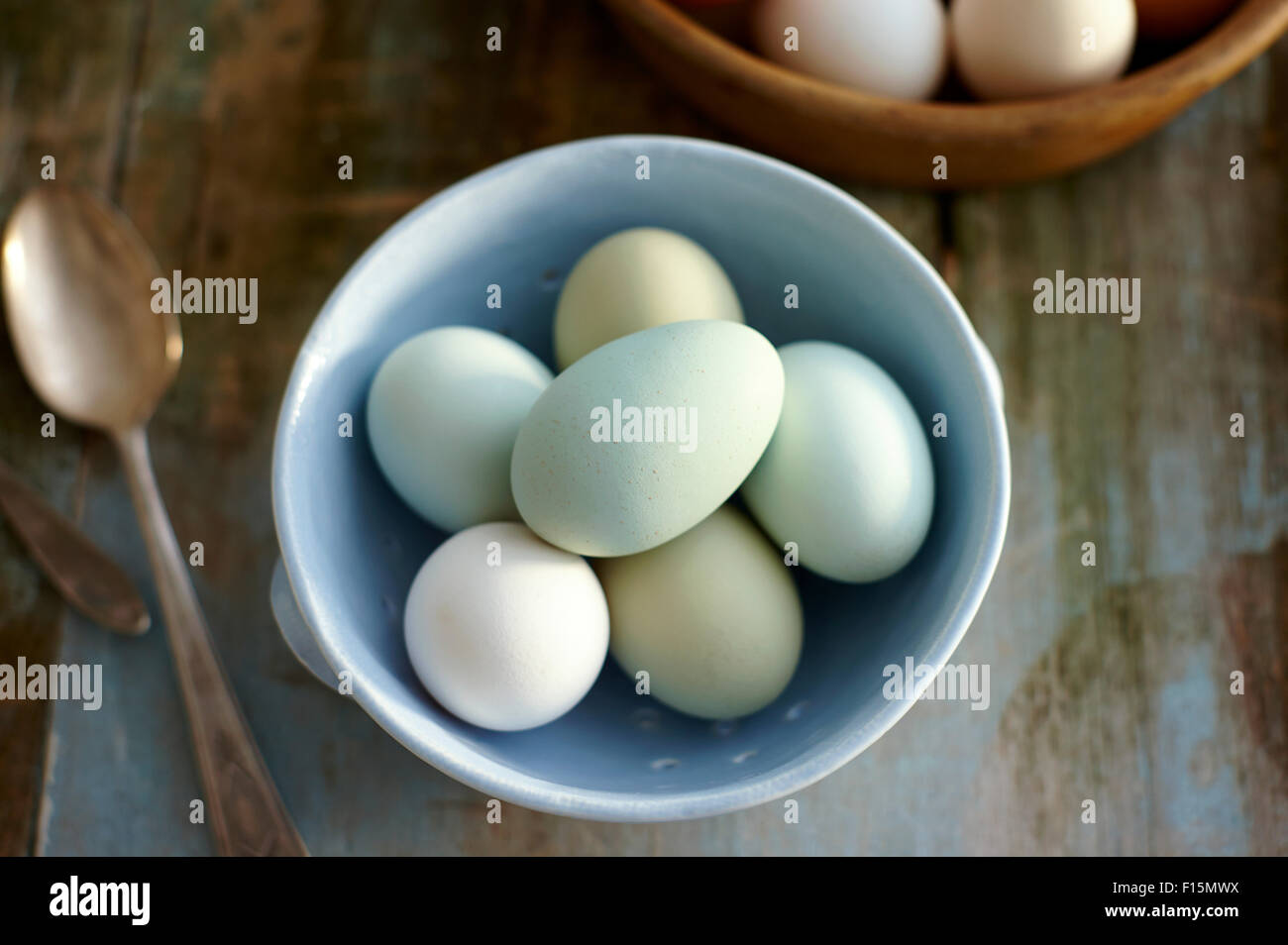 Vue de dessus de bleu, vert et blanc oeufs frais de la ferme en bleu passoire sur table en bois rustique Banque D'Images