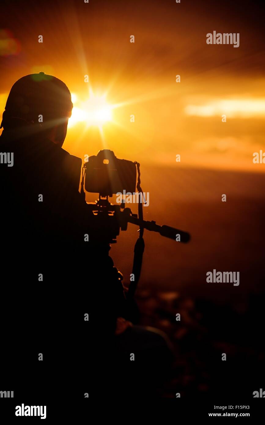 Coucher de photographe. Photographe mâle avec son appareil photo reflex numérique pour prendre des photos au coucher du soleil. Thème de la photographie. Banque D'Images
