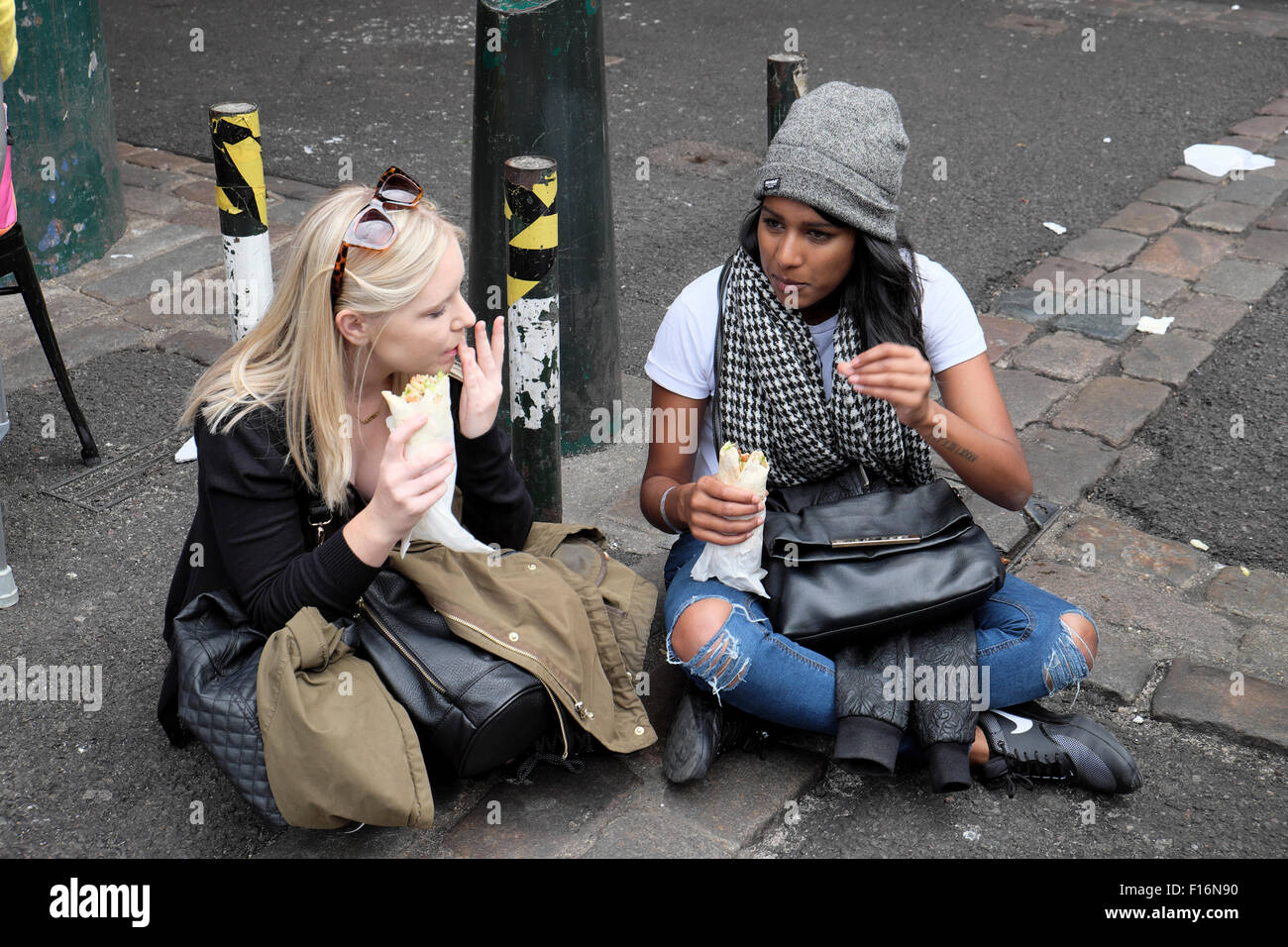 Deux amies assises ensemble parlant et mangeant des enveloppements à Borough Market à Southwark, South London UK KATHY DEWITT Banque D'Images