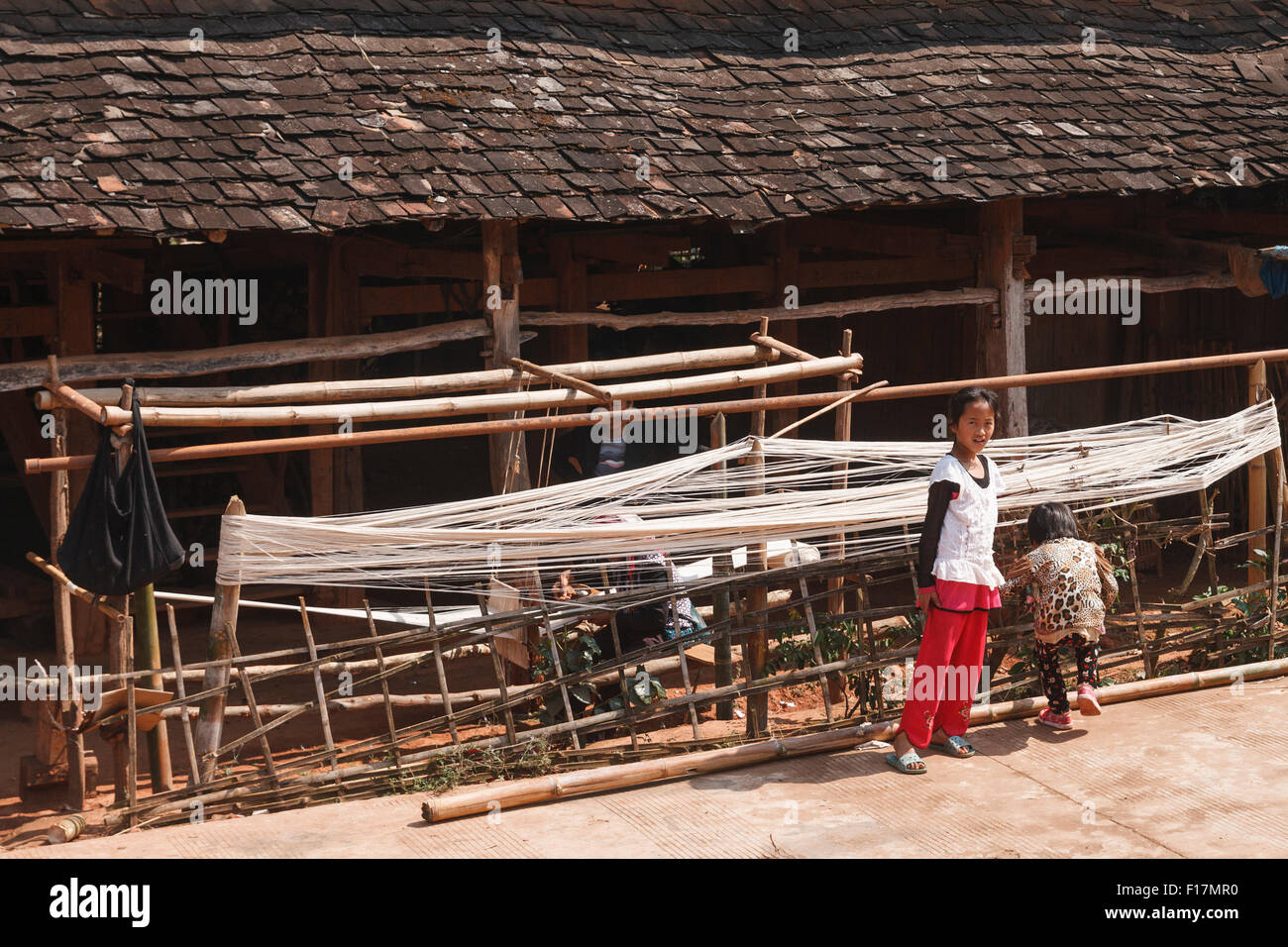 Enfants dans un village rural dans le Xishuangbanna, Yunnan, Chine, en face d'une hutte traditionnelle où le tissage et la filature lieu Banque D'Images