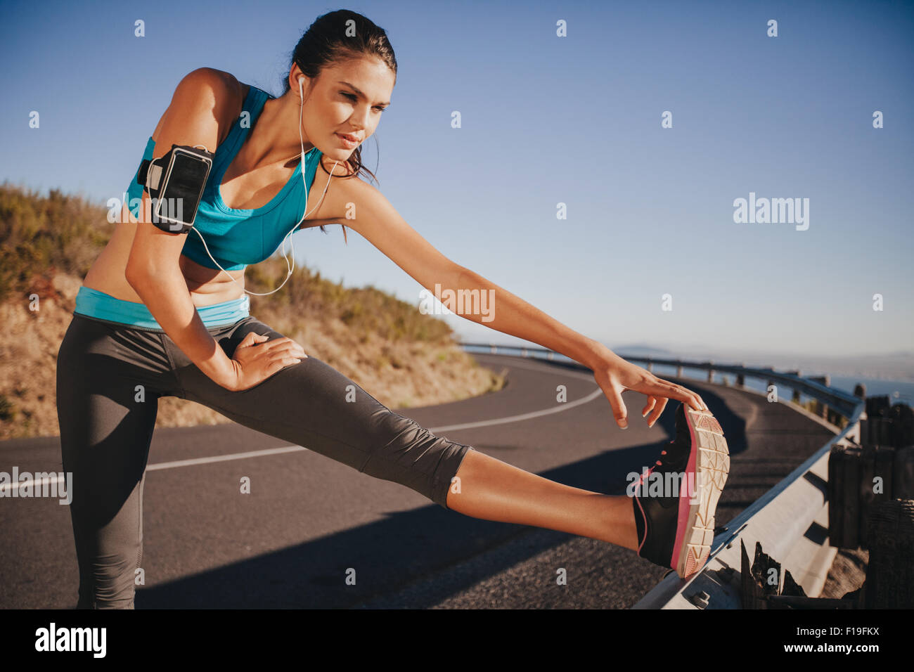 Jeune femme déterminée l'échauffement avant une course. Athlète féminin s'étend sa jambe sur la garde-corps dans la matinée. Banque D'Images