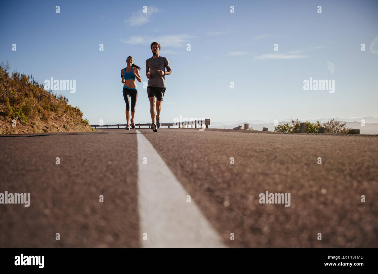Deux jeunes gens d'exécution on country road, low angle shot de coureurs sur route ouverte sur une journée d'été. Banque D'Images