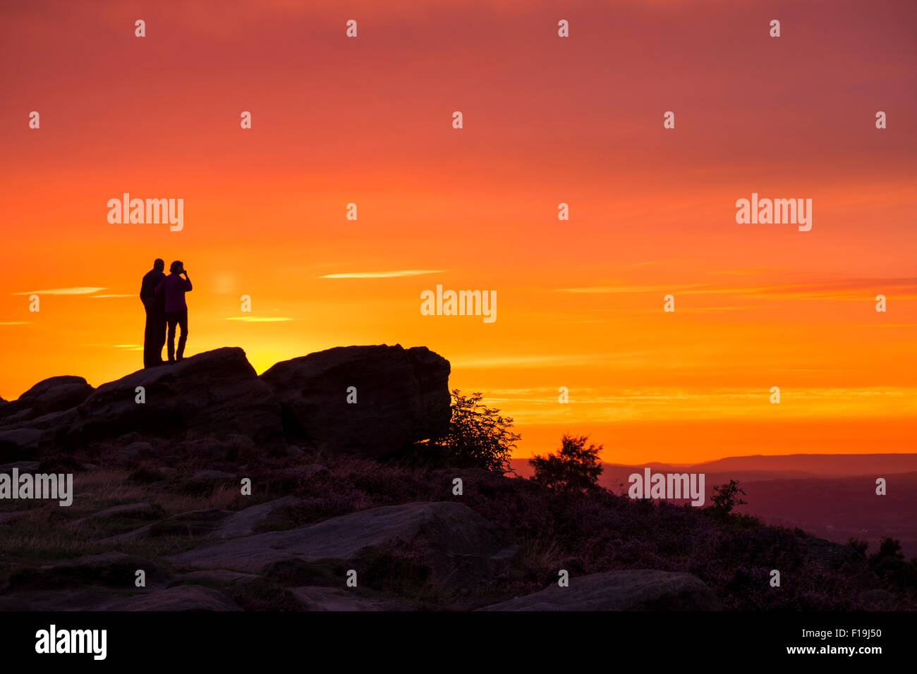 Couple debout sur les rochers à la recherche d'or au coucher du soleil orange, Otley Chevin, West Yorkshire Banque D'Images