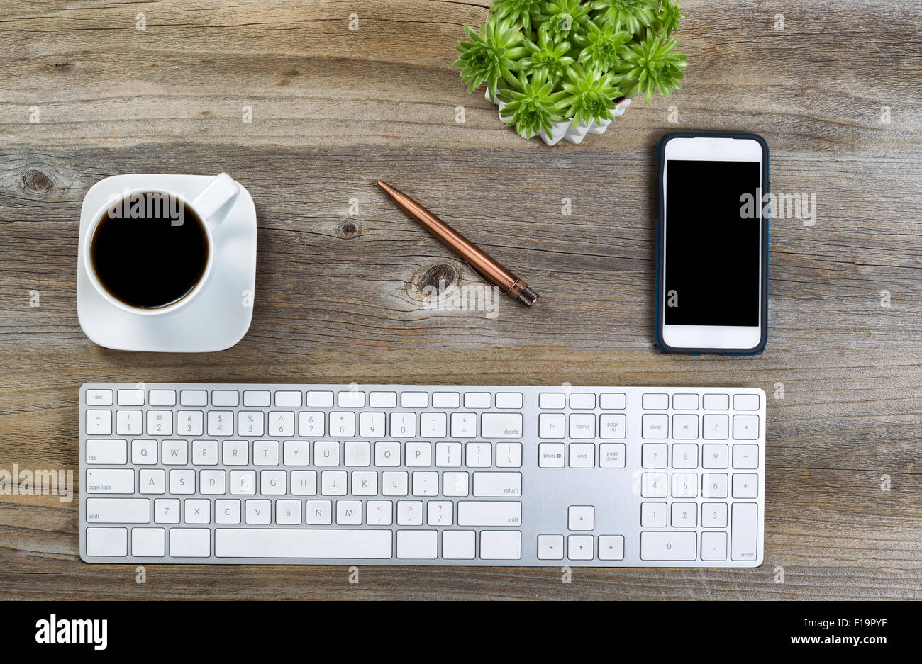 Vue de dessus d'un bureau ordonné avec clavier, un café noir, plante verte et un téléphone cellulaire sur un bureau en bois. Banque D'Images