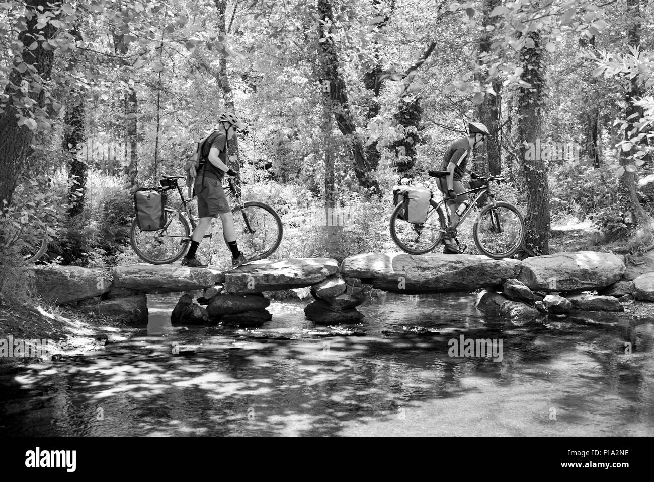 L'Espagne, Saint James Way : Biker pèlerins passant un pont de pierre sur le Camino Frances (bw) Banque D'Images