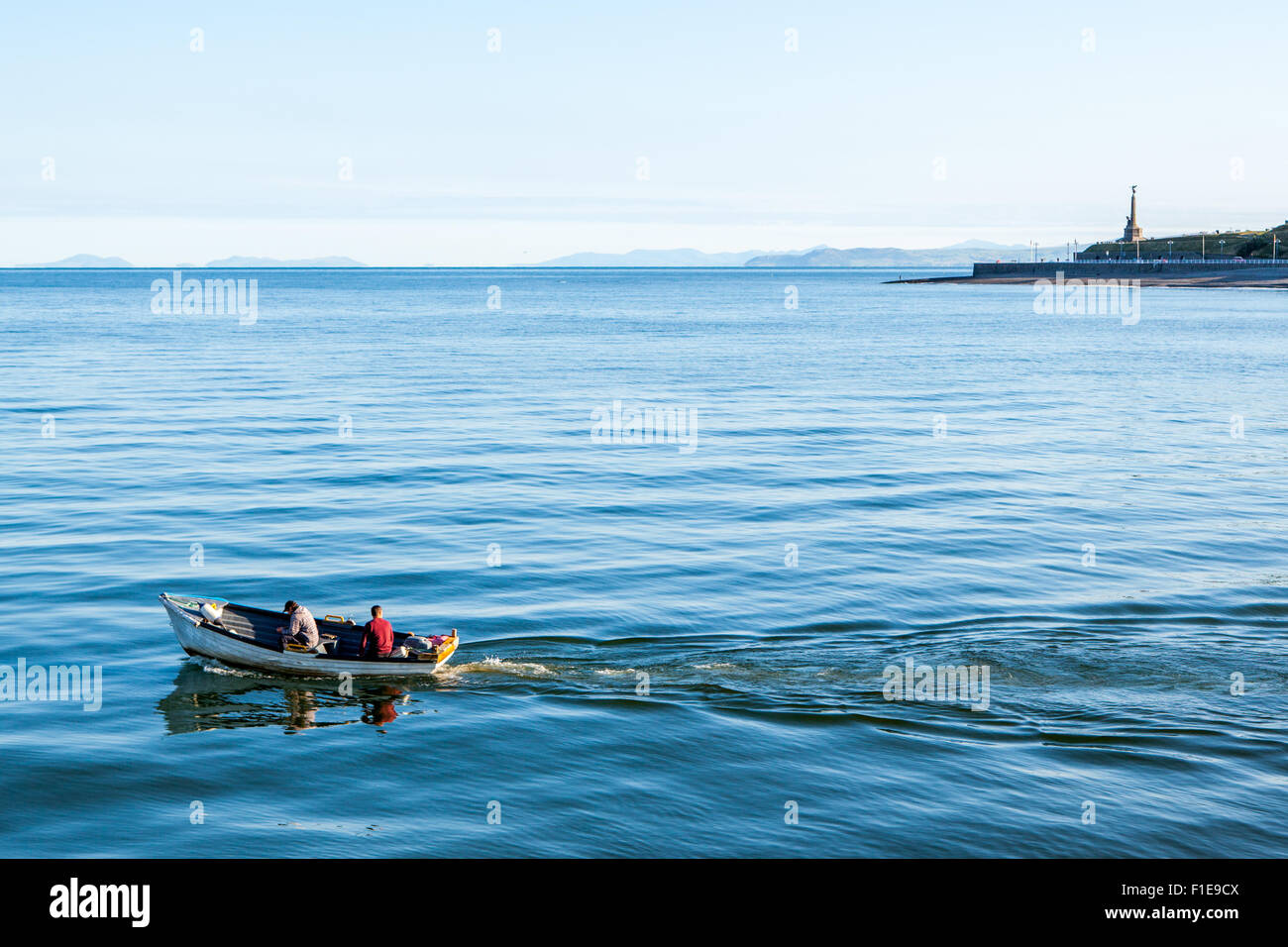 2 hommes dans un petit bateau aller en mer par un beau matin ensoleillé calme clair à Aberystwyth, Ceredigion Mid Wales UK Banque D'Images