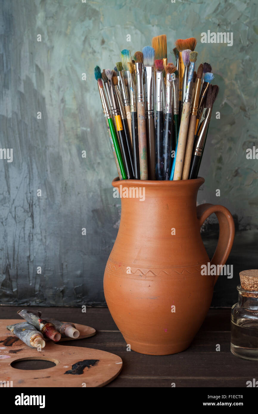 Les pinceaux dans une cruche d'argile potiers, tubes de peinture, palette et une bouteille d'huile dans un atelier d'artiste. Banque D'Images