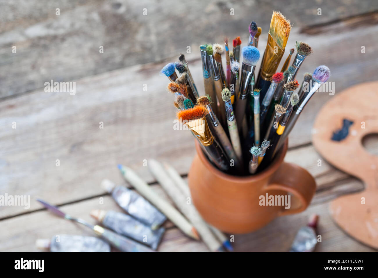 Les pinceaux dans une cruche d'argile potiers, palette et tubes de peinture sur 24. Banque D'Images