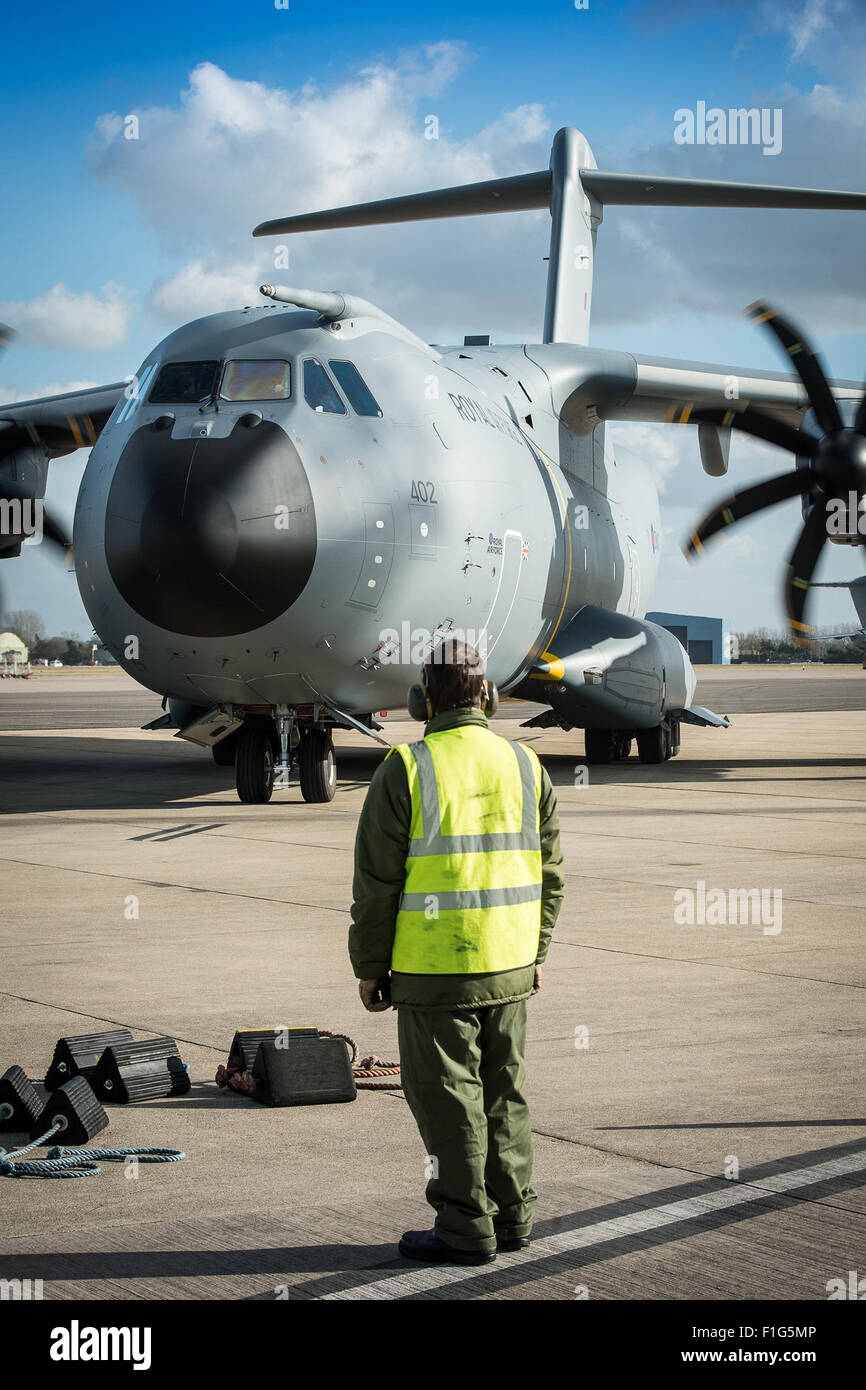 Un membre de l'équipage au sol de la Royal Air Force se prépare à installer des cales sur un avion A400M Atlas alors qu'il roule sur la piste. L'A400M est un gros avion de transport militaire, conçu pour les opérations de transport lourd, et cette scène capture un moment d'appui au sol pour ses opérations. Banque D'Images