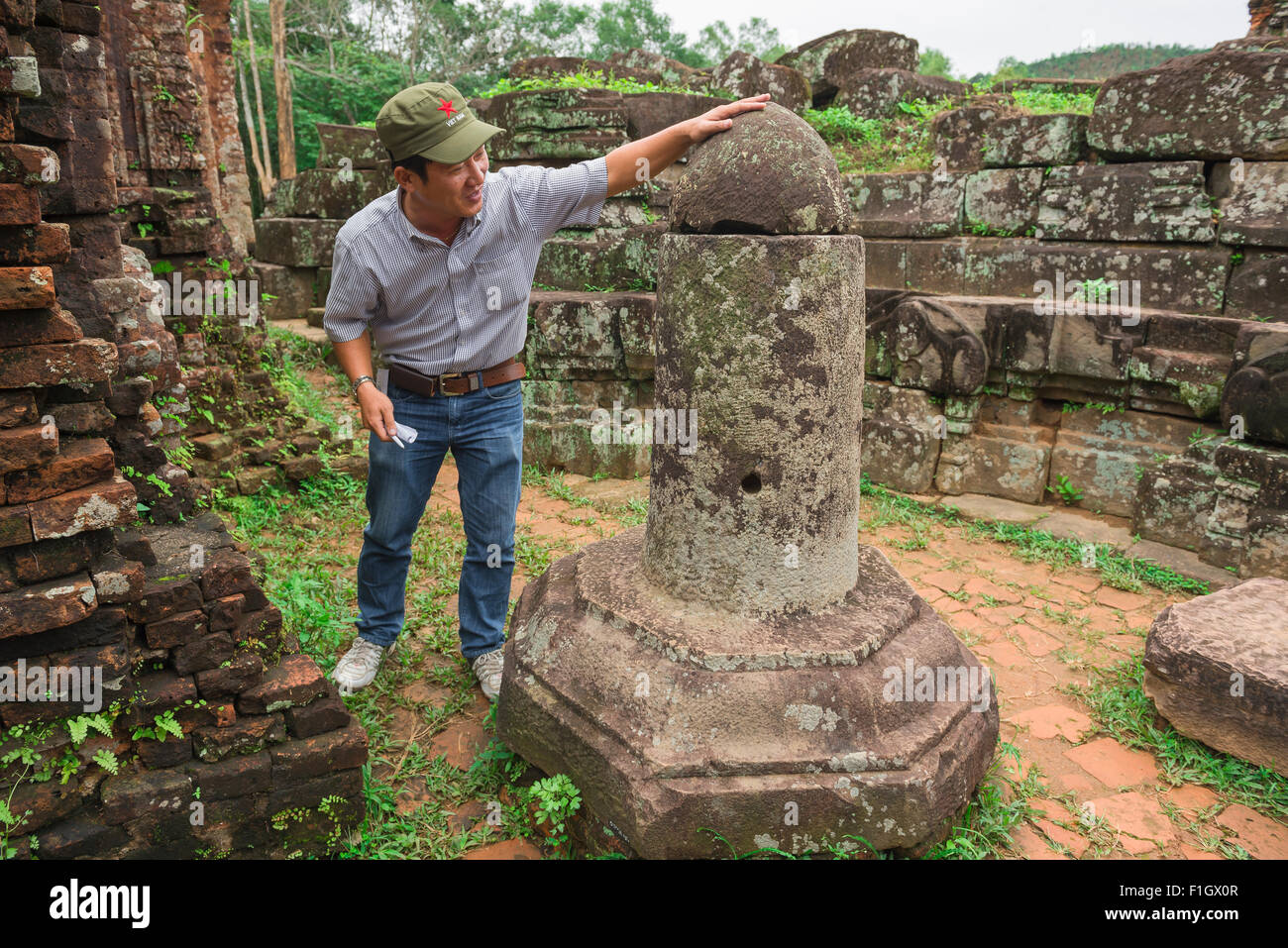 Mon fils, un guide touristique du Vietnam se trouve à côté d'un lingam en pierre à l'intérieur des ruines du temple Cham de My Son, Vietnam central. Banque D'Images
