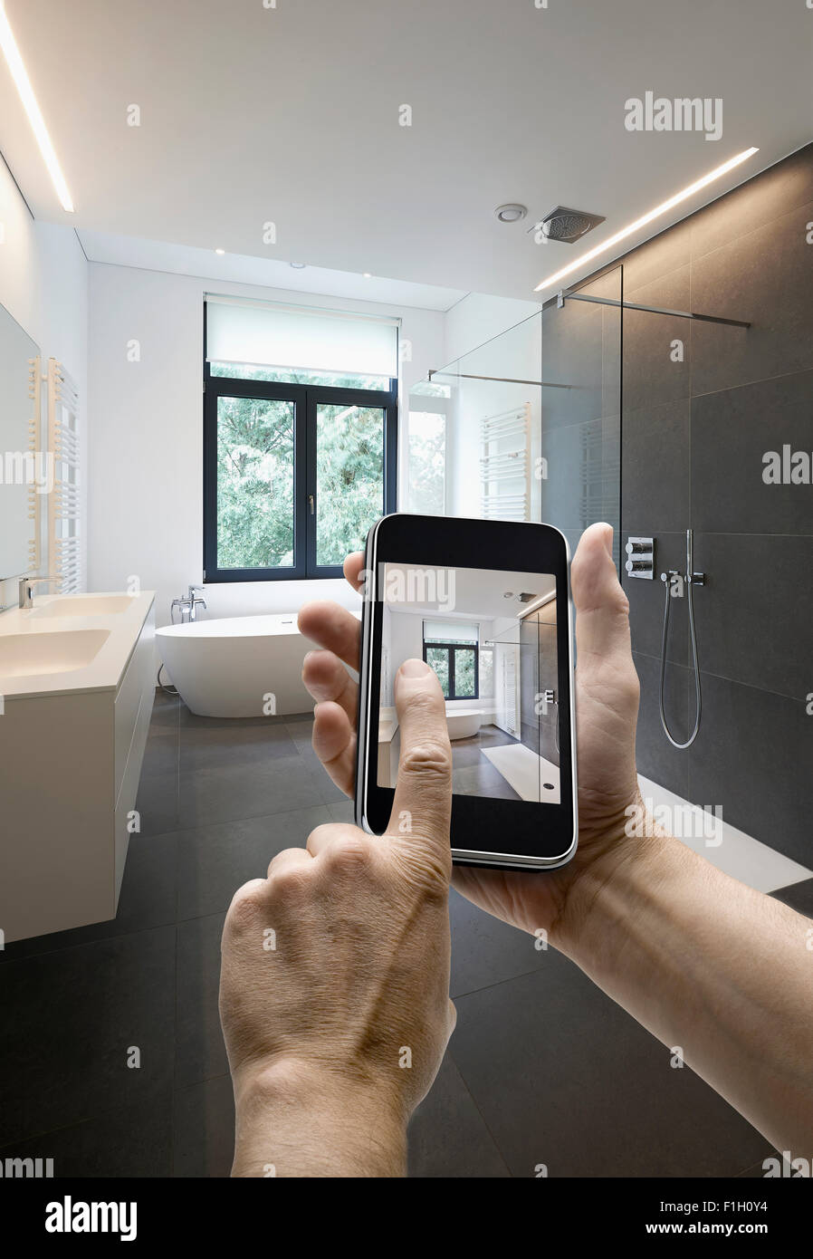 Appareil mobile avec l'homme en tenant les mains photo dans une salle de bains carrelée avec windows vers jardin, les mains sur le côté droit Banque D'Images