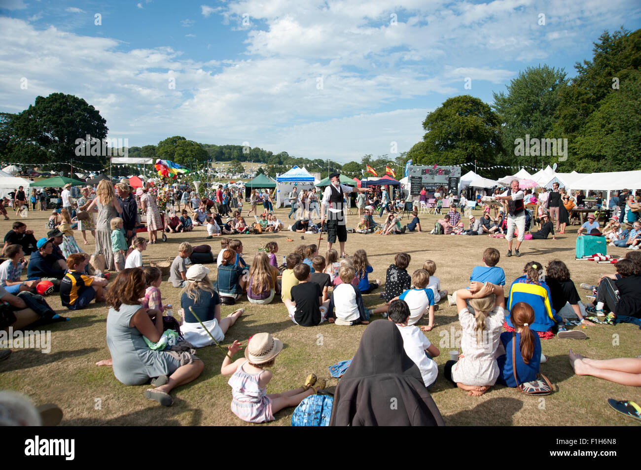 Famille regarder un acte de jonglerie dans le soleil d'été par des stands de nourriture et de tentes au Port Eliot Cornwall Festival Banque D'Images
