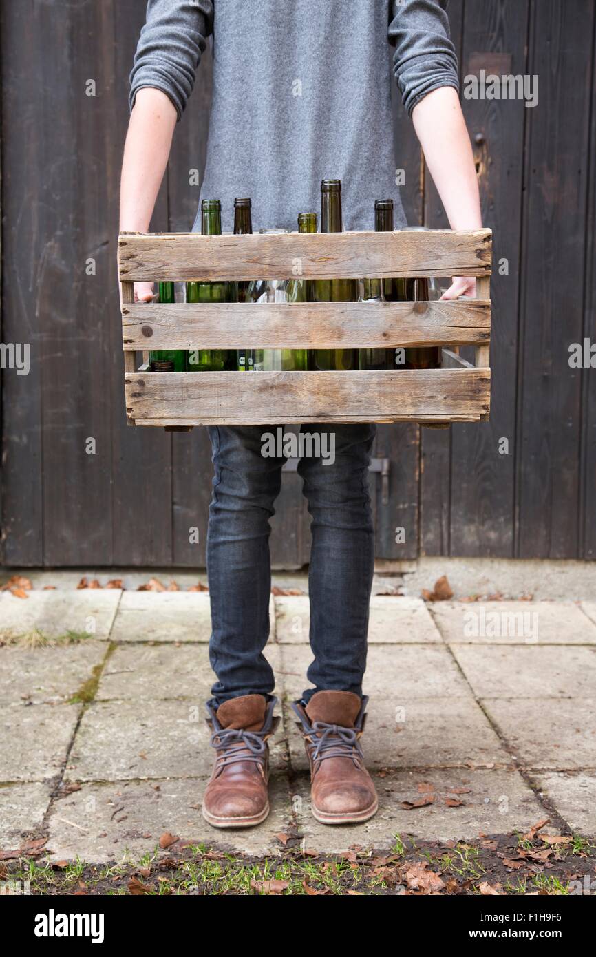 Teenage boy transportant des bouteilles vides dans des caisses en bois Banque D'Images