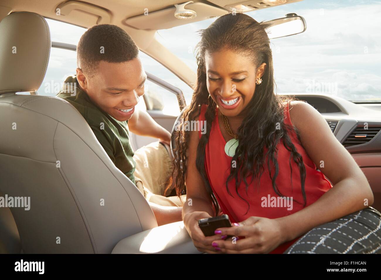 Young couple sitting in car looking at smartphone Banque D'Images