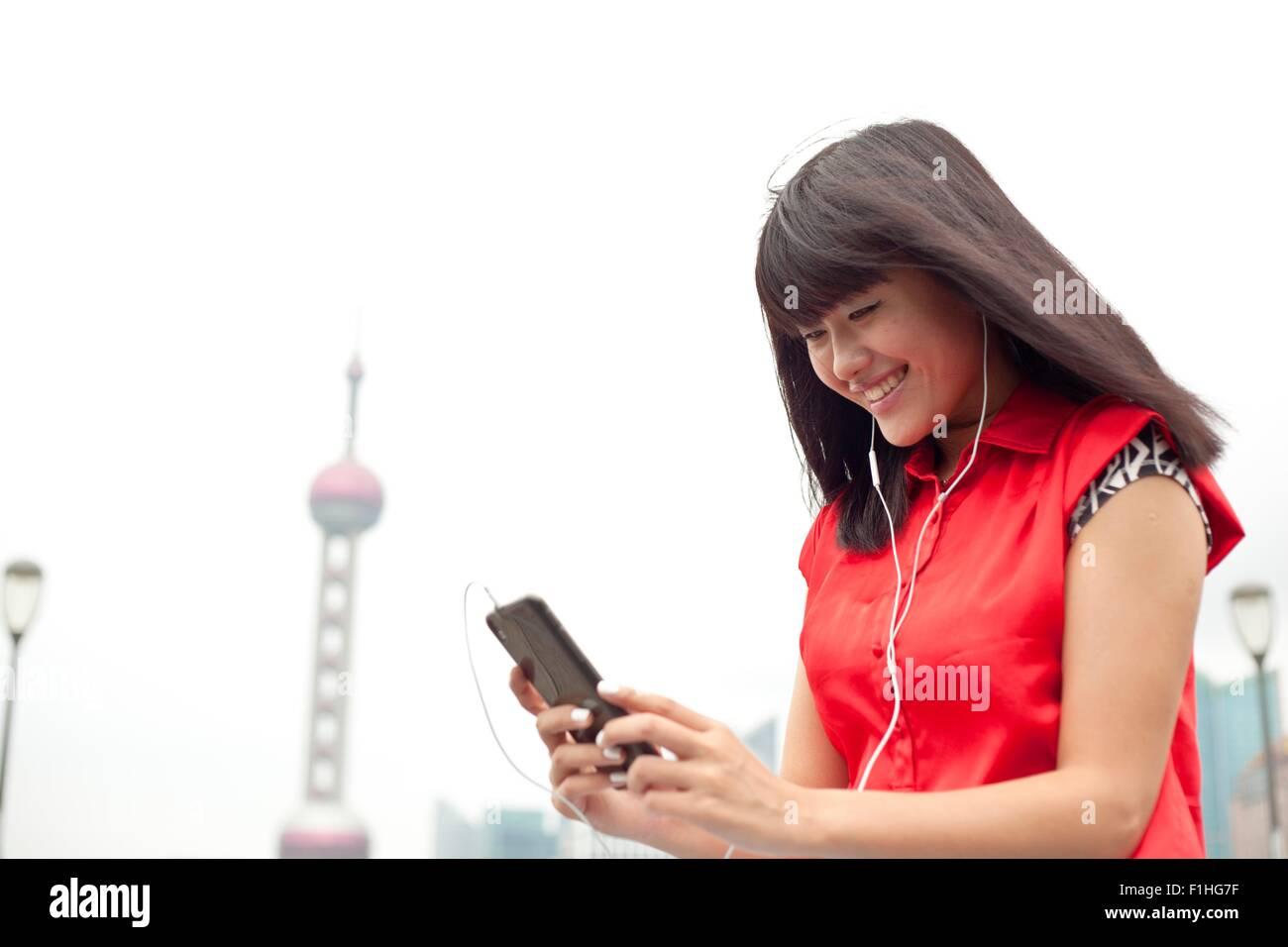 Jeune femme portant des écouteurs, looking at smartphone, Shanghai, Chine Banque D'Images