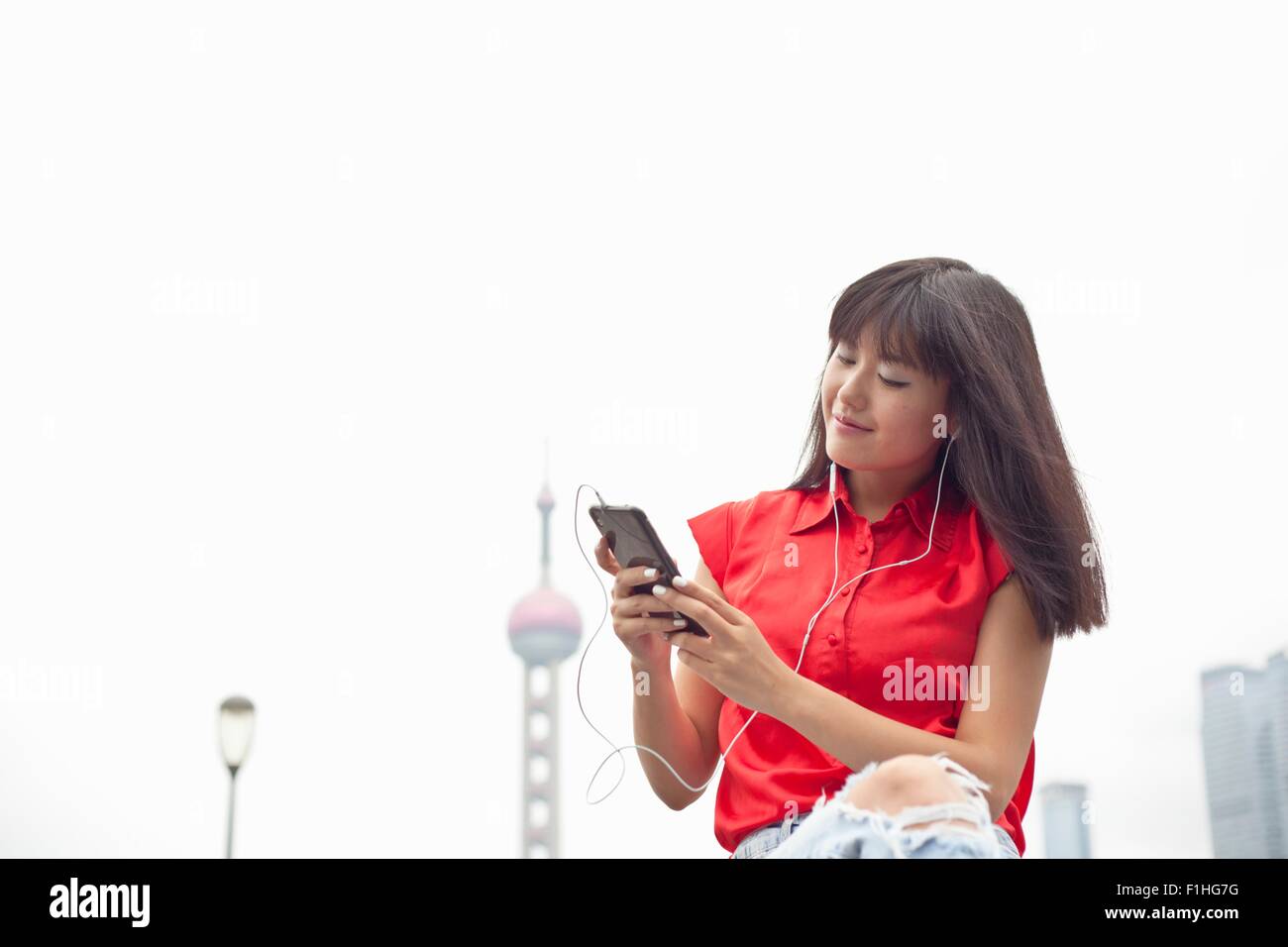 Jeune femme portant des écouteurs, looking at smartphone, Shanghai, Chine Banque D'Images