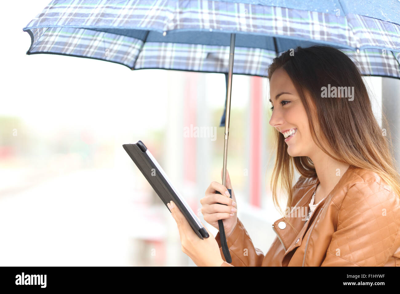 Profil d'une femme lisant ebook ou comprimé sous un parapluie un jour de pluie dans un lieu générique Banque D'Images